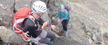 Two people rock climbing. One is helping the other belay